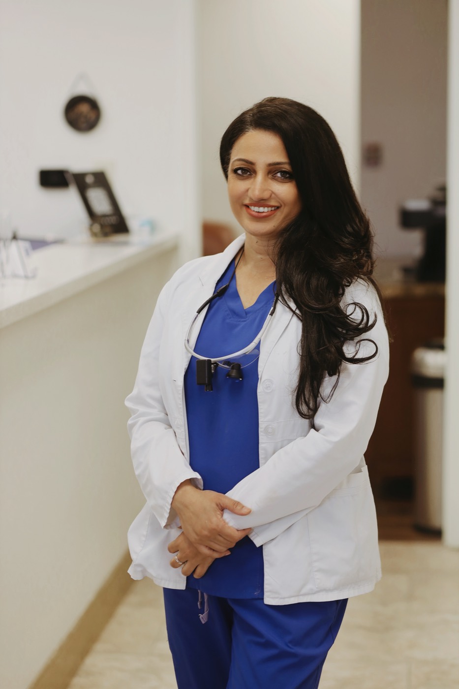 Dr. Parveen Bhatti in a white coat and blue scrubs, smiling in the office